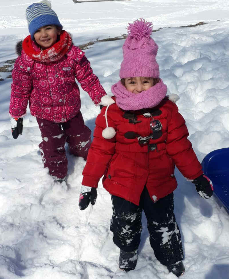 Two young girls dressed in warm winter gear smiling with background of snow